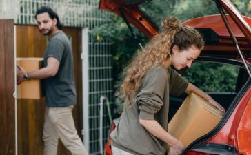 Free Multiethnic young couple in casual wear taking carton boxes out of automobile trunk near newly bought house on summer day Stock Photo