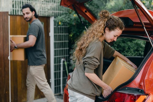 Free Multiethnic young couple in casual wear taking carton boxes out of automobile trunk near newly bought house on summer day Stock Photo